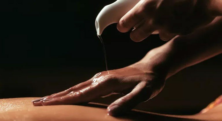 Osoba wylewa ciepły olej do masażu